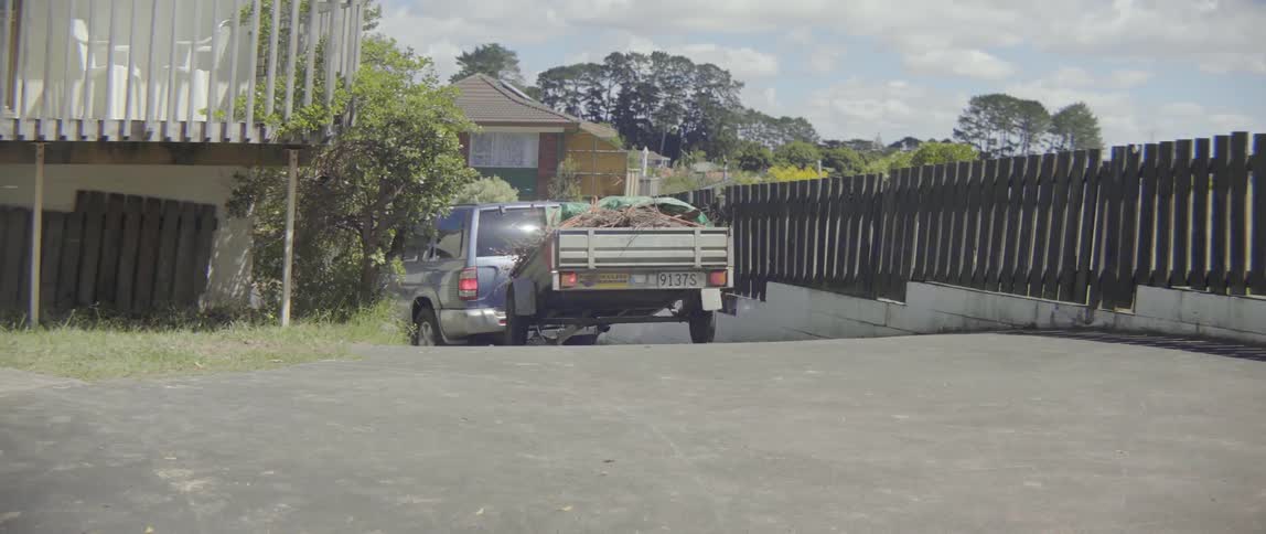 A driver transports a large pile of green waste away from a house.