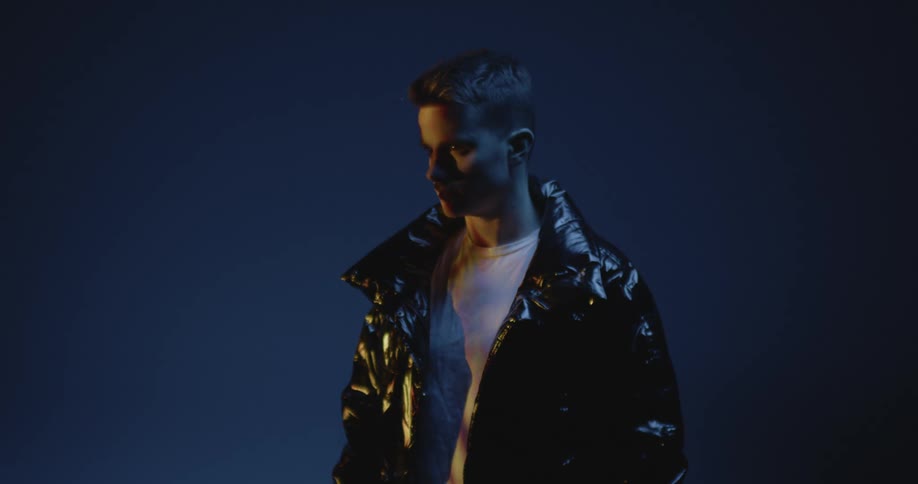 A boy wearing a leather jacket bathed in dim light
