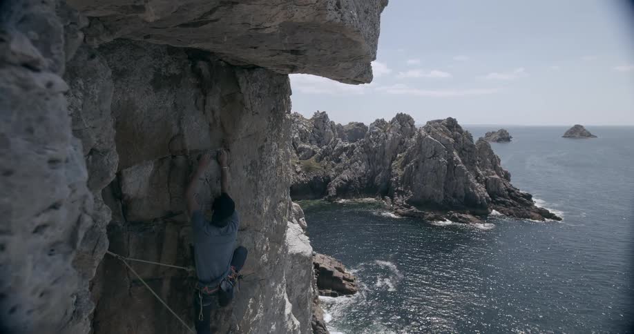 Man climbs a rock wall in the cliffs next to the ocean