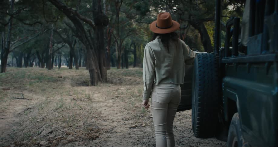 Woman wearing a hat exits a jeep in the forest
