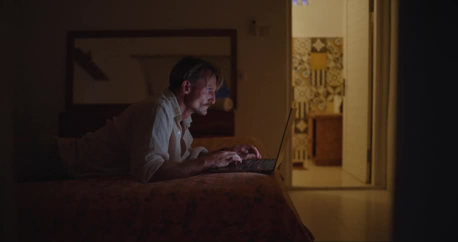 Man lying in bed working on a laptop