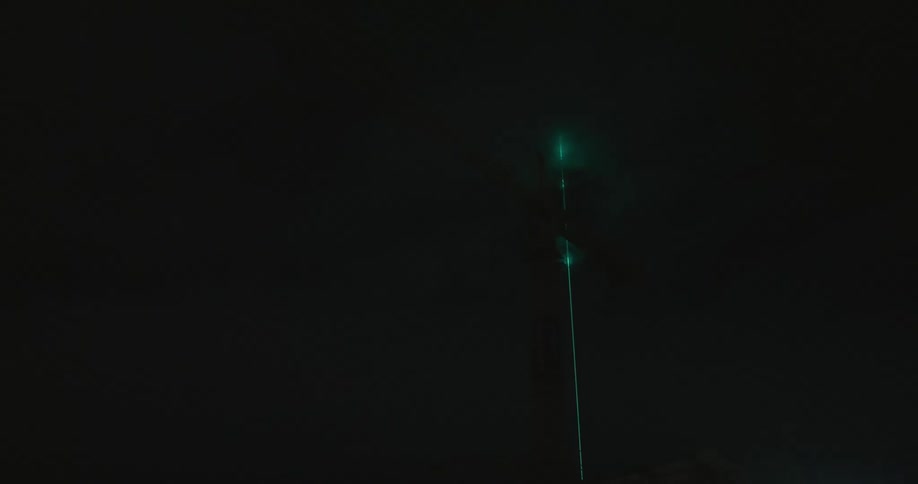 Green laser shines through the clouds at night
