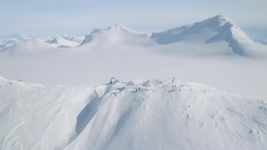Skiing on a mountain ridge covered in snow with houses buried up to the roofs on a clear sunny day