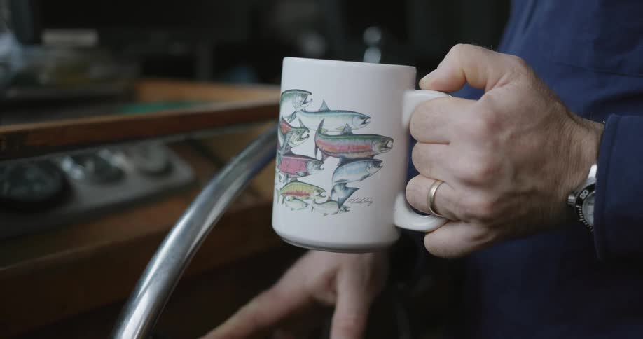 A person steers a boat while holding coffee