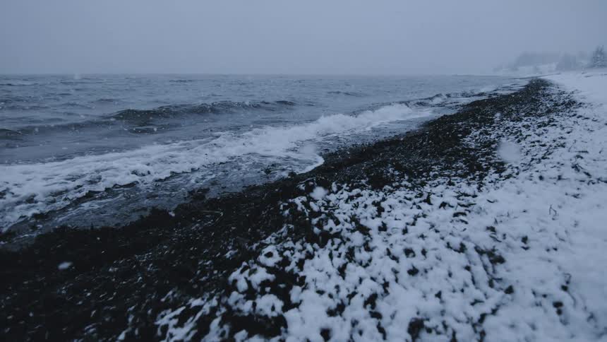 Snow falls as waves roll into shore