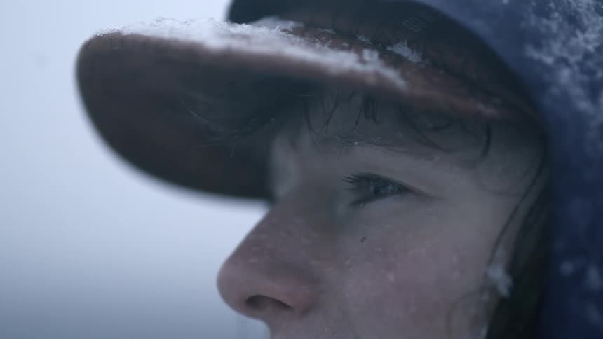 Eyes of a woman with the visor of her baseball cap covered in snow