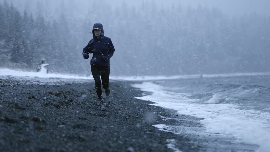 A woman running in the winter snow by the ocean