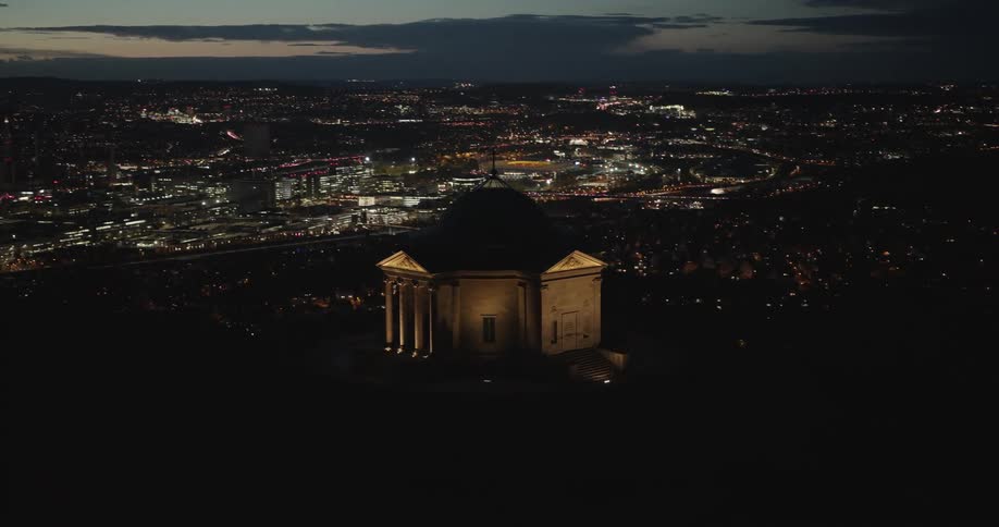 Aerial of the sepulchral chapel on wurttemberg hillin germany overlooking the city lit up at night with pink streak in the dark sky in the background