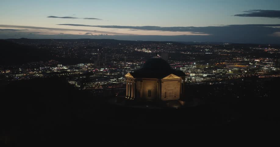 Aerial of the sepulchral chapel on wurttemberg hillin germany overlooking the city lit up at night with pink streak in the dark sky in the background