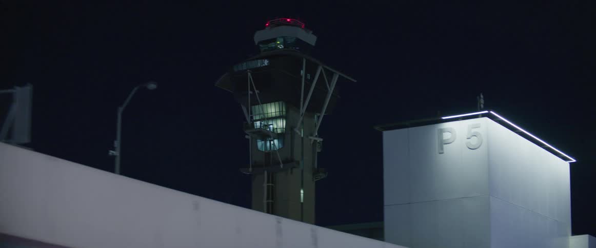 Air traffic control tower towers over airport terminal with a pedestrian bridge and a parking garage