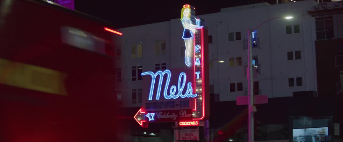 Neon lights flash on sign in front of mels bar as an ambulance drives past