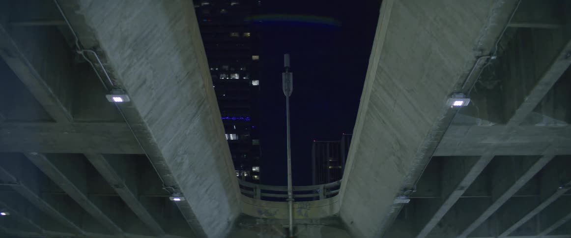 The underside of a concrete bridge with lights and a building in the background