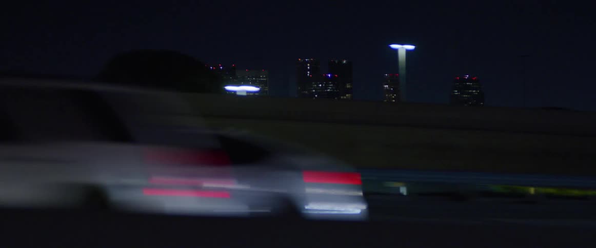 Car lights blur past on a freeway drive at night with the city skyline in the backgound