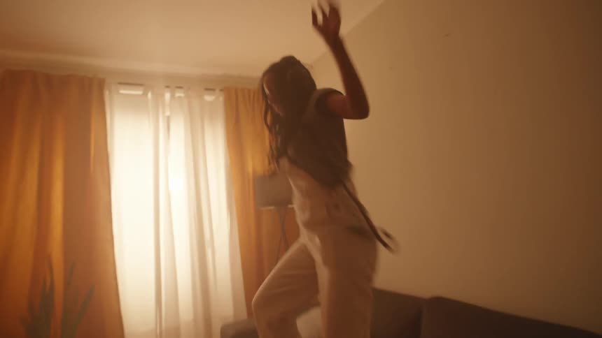 Happy woman listening to music dances over the couch in the living room