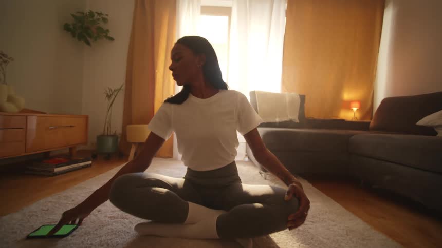 Woman sitting on the living room floor meditating picks up her phone