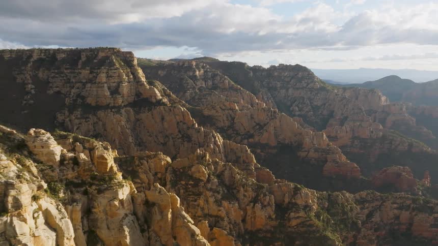 The sun shines upon mountains and rock formations under a cloudy sky