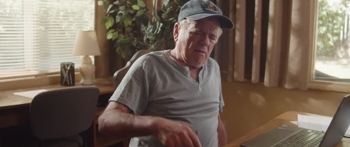 Elderly man sitting in front of laptop opens a notebook before viewing computer screen