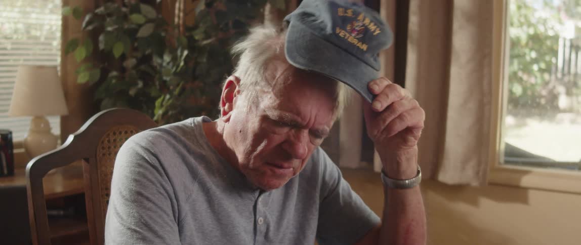 Elderly man sitting at home takes off his baseball cap