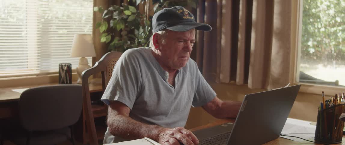 Elderly man flips quickly through notebook while doing paperwork at home then gestures angrily