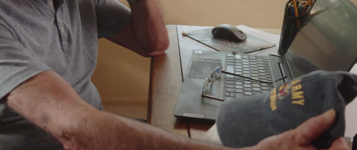 An elderly man sitting at a table holding a hat