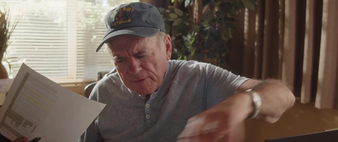 An elderly man is sitting at a table with a laptop computer going through paperwork