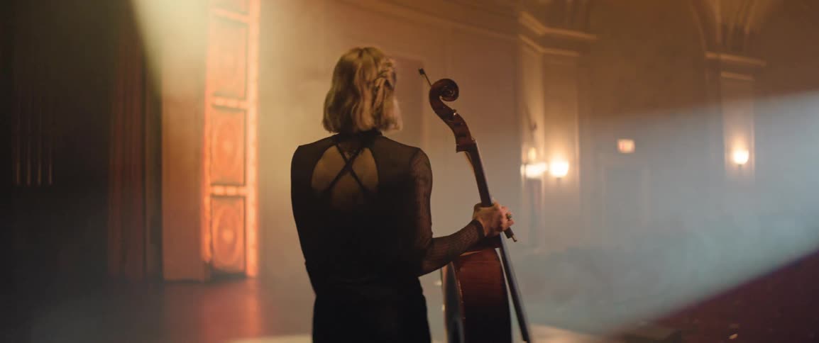 Musician carries a cello onto the stage of a theater entering the spotlight