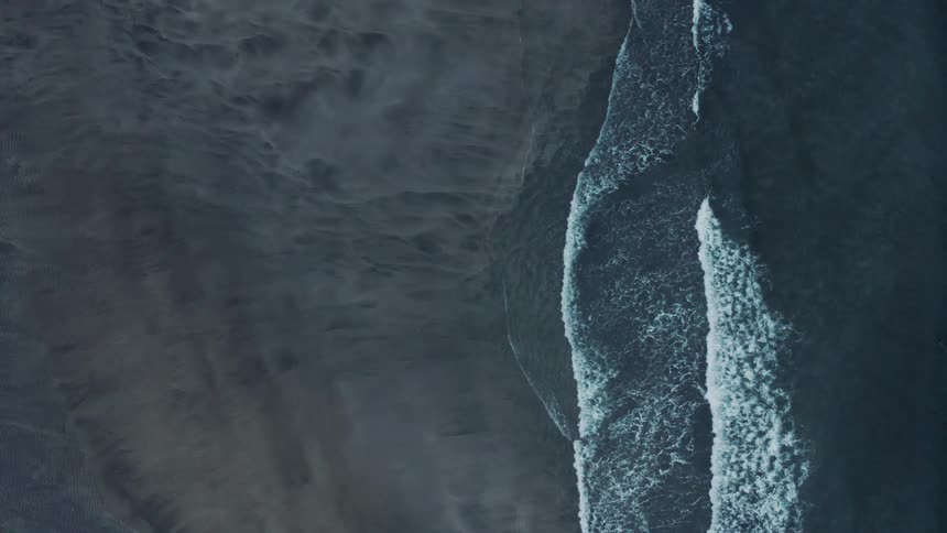 Aerial of ocean waves rolling into the sandy shoreline