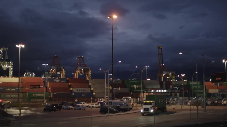 View of cars and a truck next to containers at a port