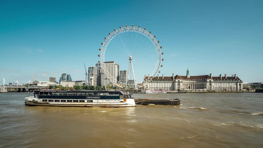 A ferris wheel is spinning and a vessel in the water is still while others are moving
