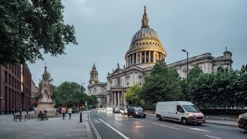 Vehicles and pedestrians move along street past domed landmark building as night falls
