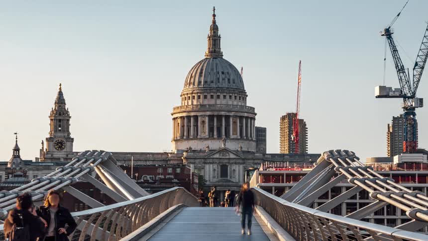 Pedestrians walk across bridge toward domed building near a construction site