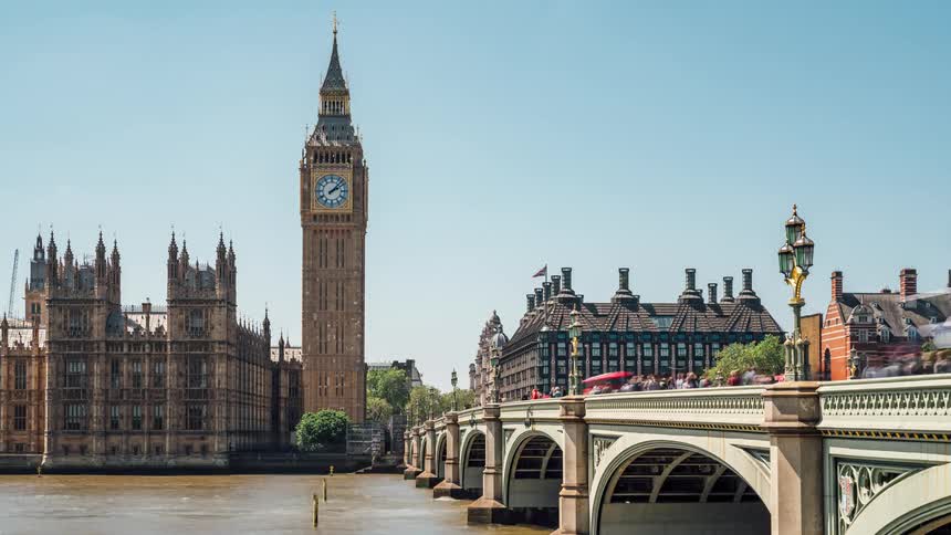 A bridge that goes over a canal and there is a large tower with a clock on top