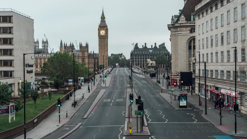 A street with many vehicles passing in time lapse near a building with a clock on top