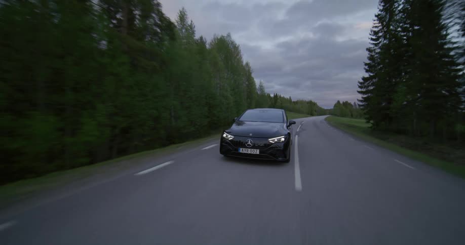 Aerial of a black car driving on a country road near a green forest