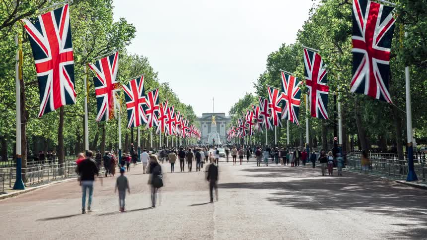 Visitors stroll up and down buckingham palace road with british flags elegantly hanging in the air