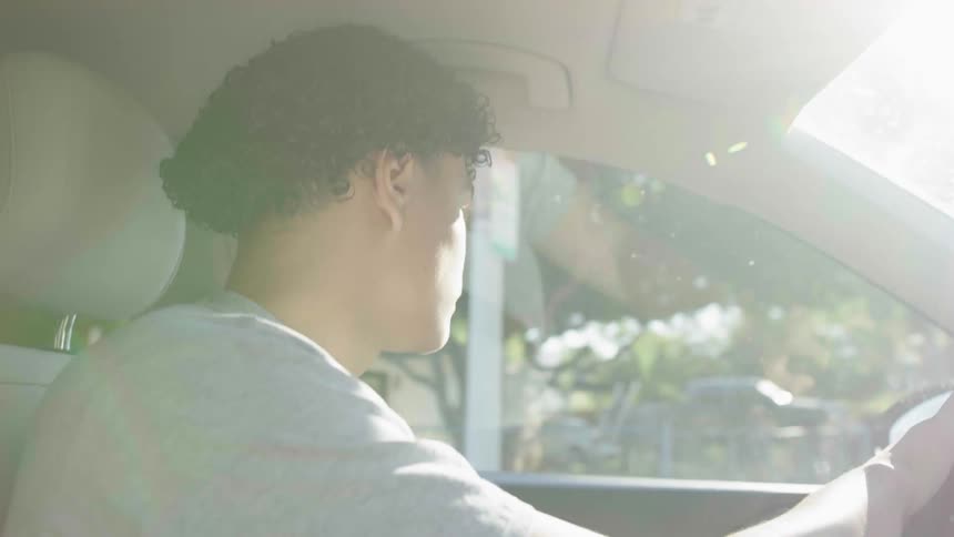A young man is driving a car and sunlight is on his face