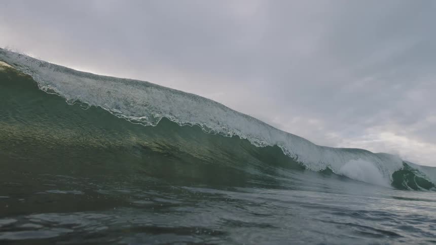 A powerful wave in the ocean under a cloudy sky