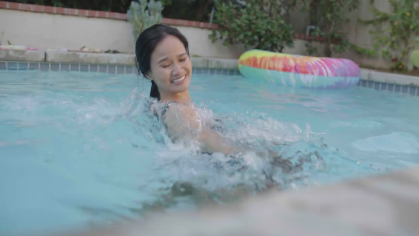 A woman dunks a mans head under the pool water