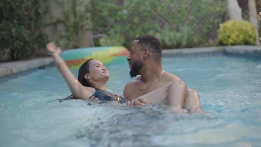 Bearded man and woman in a black swimwear play with one another n the swimming pool