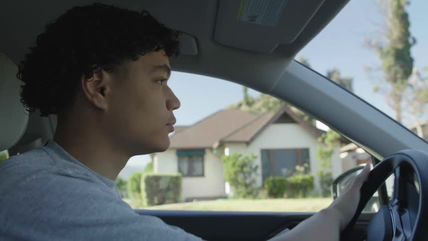 A young man drives a car and looks both ways at an intersection