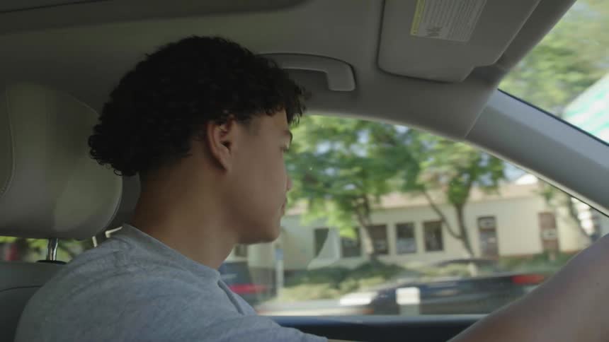 A young boy is driving a car and looks out the window