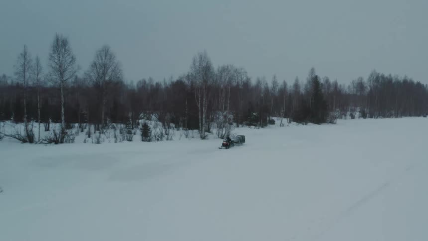 Person riding a snowmobile through the snow next to a forest on a cloudy day