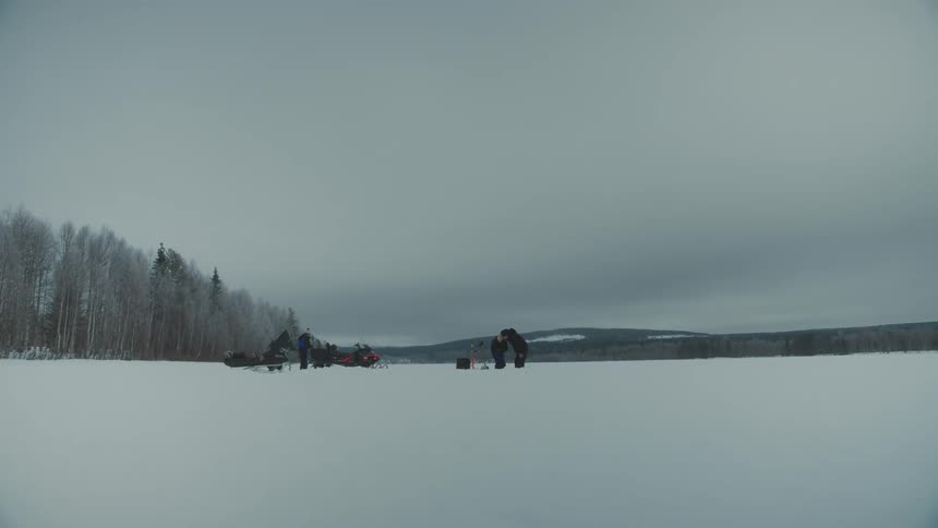View of snowcovered ground next to a forest with people in the background on a cloudy day