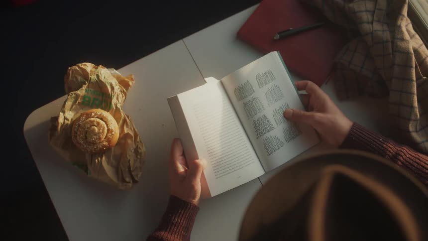 A clip of a man reading a book and a doughnut on the table