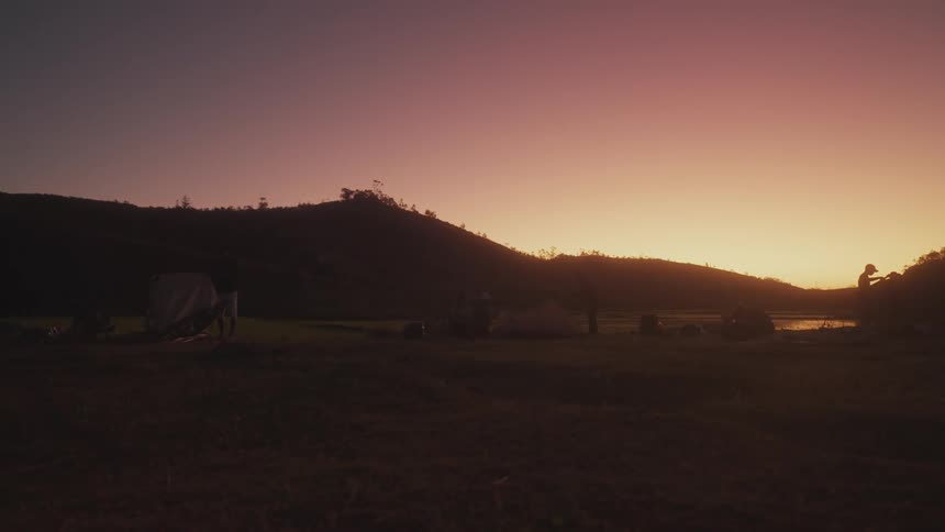 A group of people are camping as the sun is set below the nearby hills