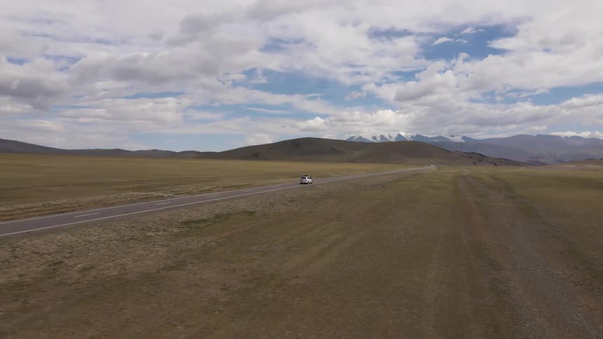Aerial of a car driving on a deserted road in the natural landscape with plains and mountains