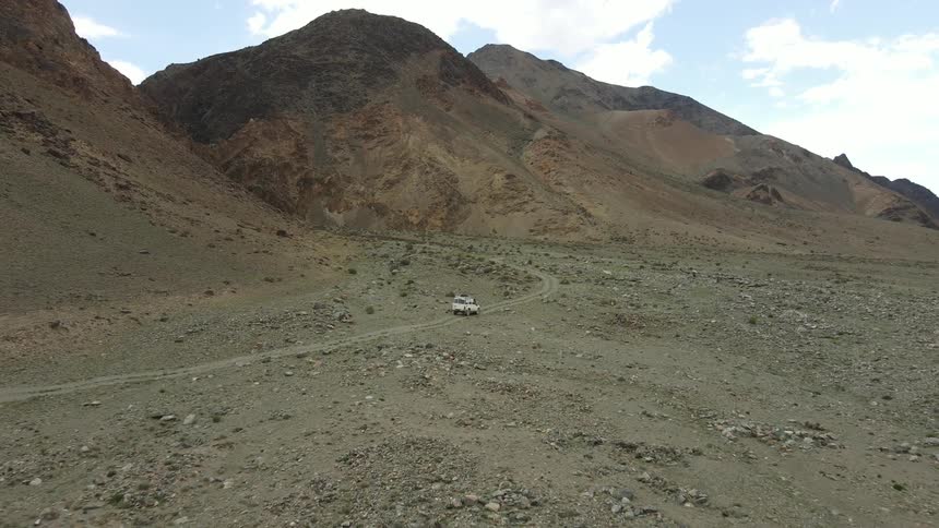 A white suv travels along a dirt road in a remote mountainous desert on a partly cloudy day