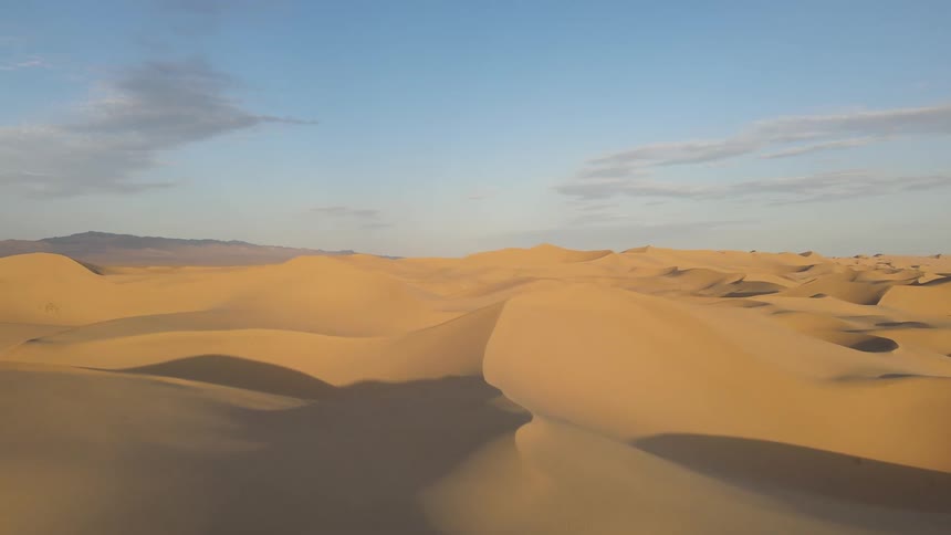 Sand dunes cast shadows onto hollows in sandy desert on a cloudy day