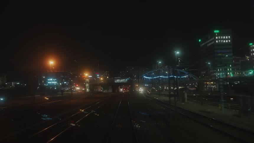 Rear window on train car reflects lights as train passes through city at night