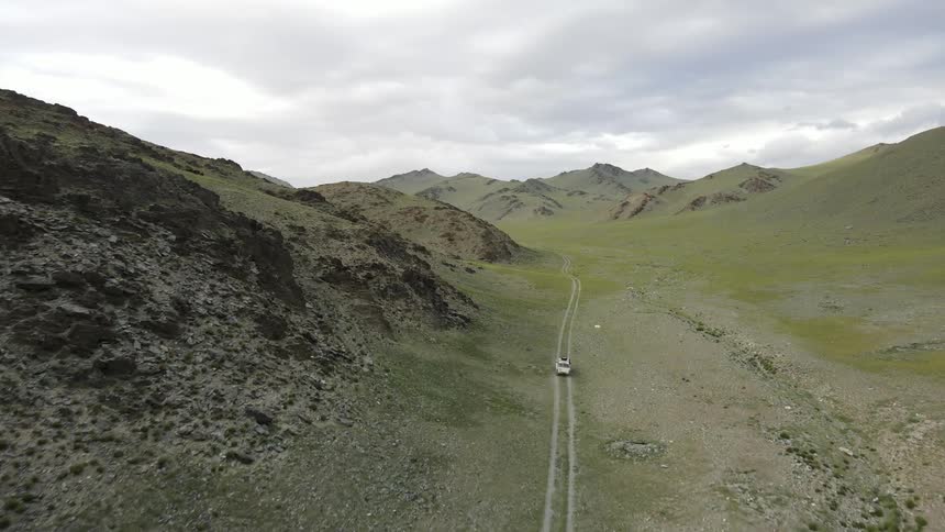 Vehicle drives along dirt road through valley between mountains on an overcast sky